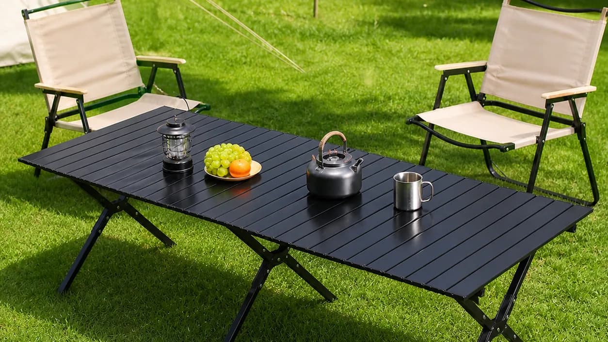 A Fuyao folding camp table and chairs set up on grass by a lake